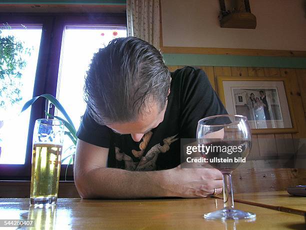 Symbol Alkoholismus, Depressionen, alkoholisierter Mann sitzt am Tisch mit Wein und Bier