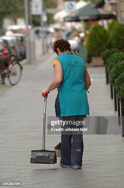Deutschland , Berlin, Mitte - Friedrichstrasse.Vor dem Q206 in der Friedrich-Ecke Taubenstrasse fegt eine Frau im Kittel Abfall weg
