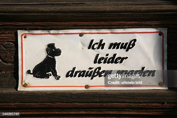 Schild mit der Aufschrift "Ich muss leider draußen warten" und einem stilisierten Pudel an einer Tür