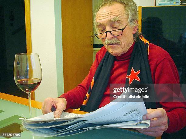 Rentner mit Lesebrille und einem roten Stern auf dem Schal liest die Zeitung