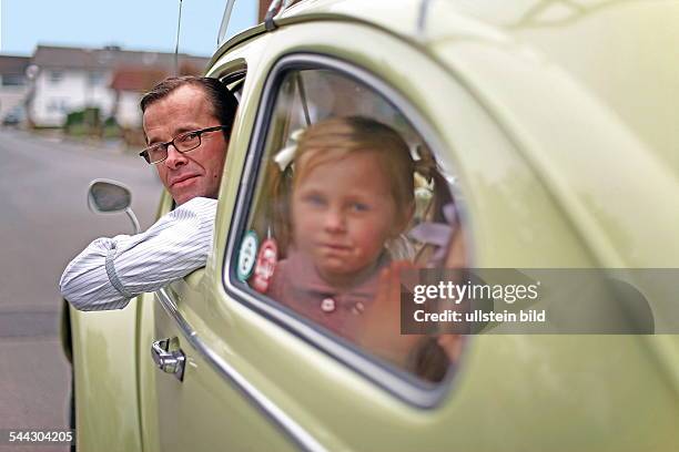 Familienfoto im Stil der 50er-Jahre. Der Volkswagen Baujahr 1955 steht im Mittelpunkt. Szene: Blondes Mädchen mit Zöpfen posiert vor dem Auto,...