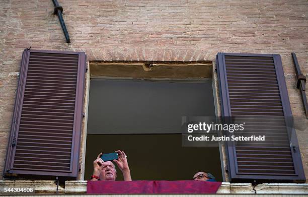 Former King Juan Carlos of Spain takes a picture from a balcony during the historical Italian horse race of the Palio Di Siena on July 02, 2016 in...