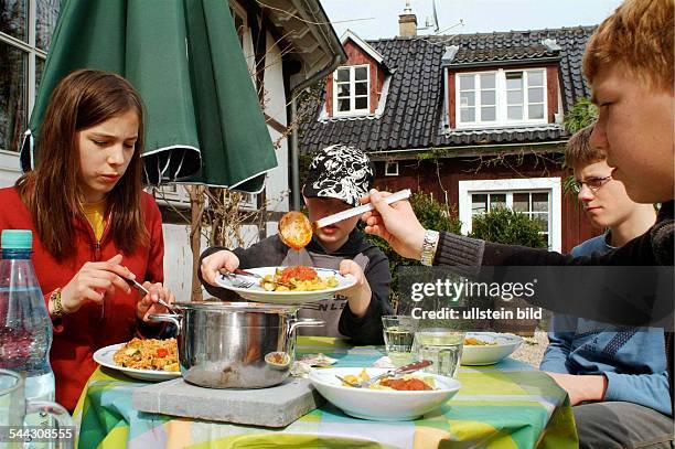 Deutschland, Kinder / Jugendliche beim Servieren des selbstgekochten Mittagessens im Garten hinter dem Haus. Es gibt Tortellini oder Reis mit roter...