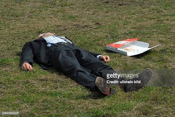 Deutschland, Berlin - Mitte. Mittagspause, Mann im Anzug liegt auf dem Rasen und sonnt sich. Neben ihm eine leere Pizzaverpackung.
