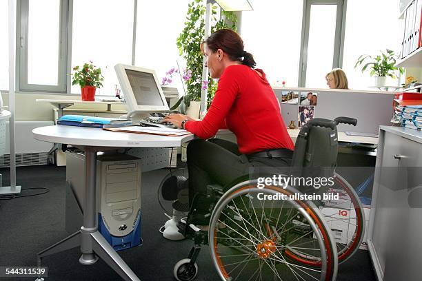 Behinderte, Frau im Rollstuhl arbeitet am Computer in einem Buero, handicapped person in a wheel chair working in the office