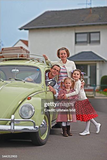 Familienfoto im Stil der 50er-Jahre. Der Volkswagen Baujahr 1955 steht im Mittelpunkt. Szene: Vater, Mutter und drei Kinder posieren stolz vor dem...