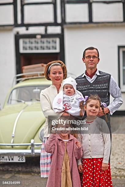 Familienfoto im Stil der 50er-Jahre. Der Volkswagen Baujahr 1955 steht im Mittelpunkt. Szene: Vater, Mutter und drei Kinder posieren stolz vor dem...