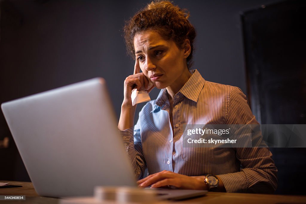 Sad businesswoman in the office working on laptop.