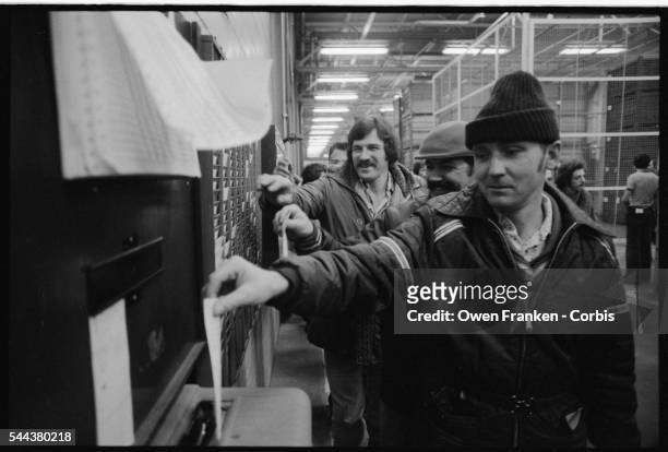 Auto workers punch their time cards at the clock in a Montreal factory.