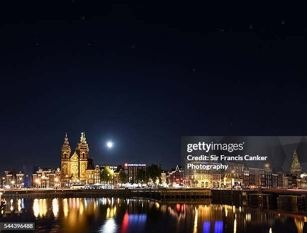 amsterdam skyline illuminated at night with full moon and reflection on amstel river, the netherlands - amstel stockfoto's en -beelden