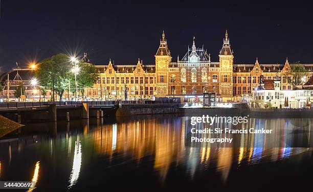 amsterdam central station illuminated at night and reflected on canal waters, the netherlands - amsterdam night stock-fotos und bilder