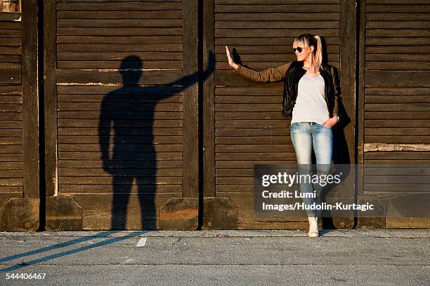 young woman gesturing with silhouette of young man against wooden wall - sillouette cool attitude stock pictures, royalty-free photos & images