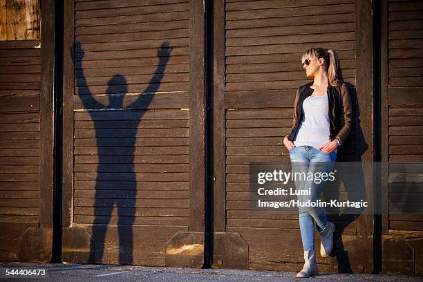 young woman alongside silhouette of young man against wooden wall - sillouette cool attitude stock pictures, royalty-free photos & images