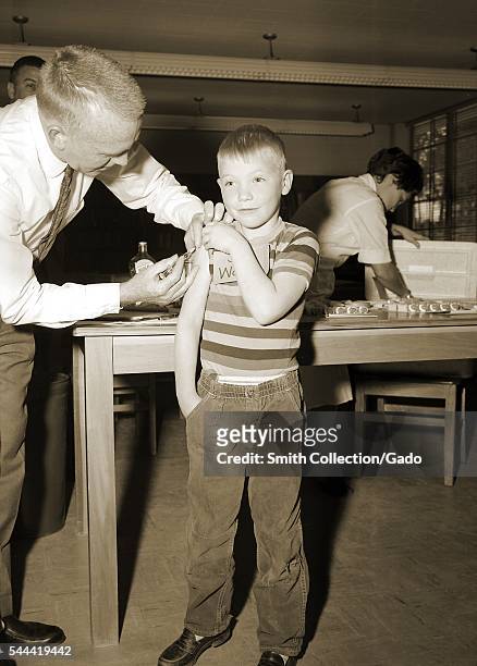 This 1962 image depicts a schoolboy receiving a measles vaccination, 1962. As part of the national immunization effort, this doctor was giving a...
