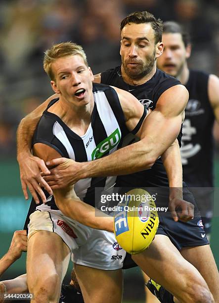 Josh Smith of the Magpies handballs whilst being tackled by Andrew Walker of the Blues during the round 15 AFL match between the Carlton Blues and...