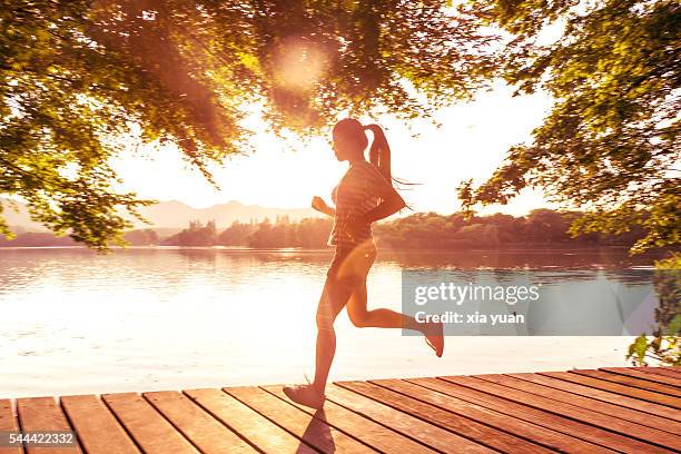 young asian woman running on pier against lake at sunset - beautiful underwater scene stockfoto's en -beelden