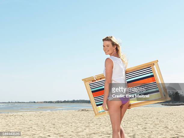 young woman carrying deck chair on beach, altona, melbourne, victoria, australia - beach deck chairs stock pictures, royalty-free photos & images
