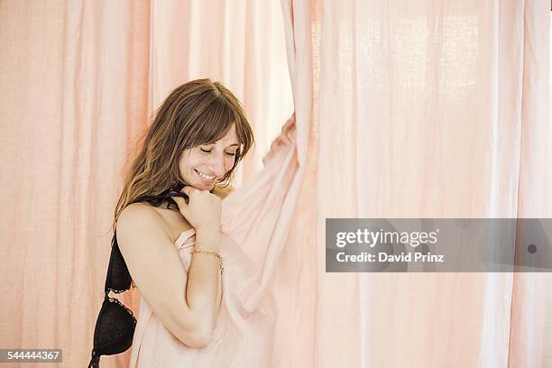 portrait of shy mid adult woman undressing in boutique changing room - bra stock pictures, royalty-free photos & images