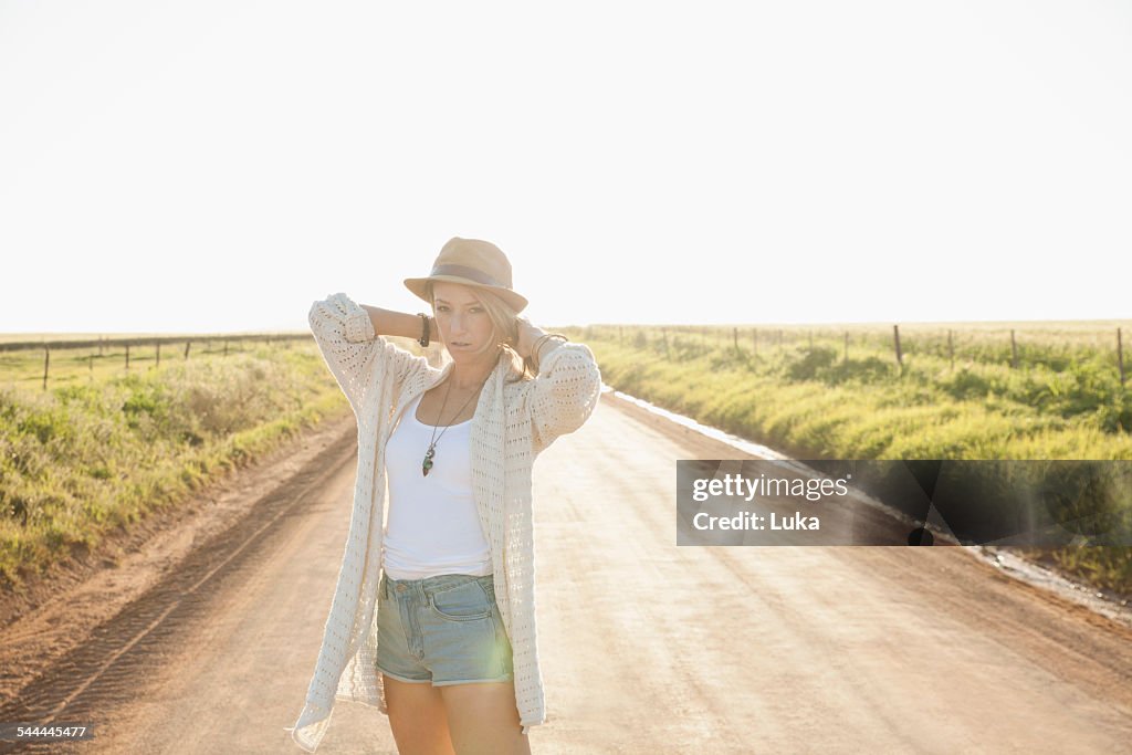 Mid adult woman on country road, arms behind neck, looking at camera