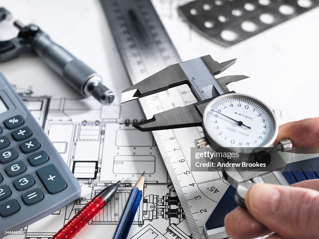 Engineer holding dial caliper with measurement equipment sitting on technical drawing