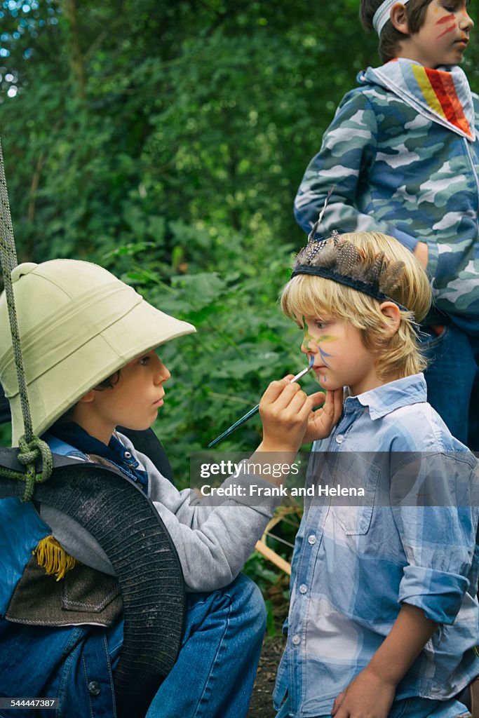 Three boys playing dress up in forest with face paint