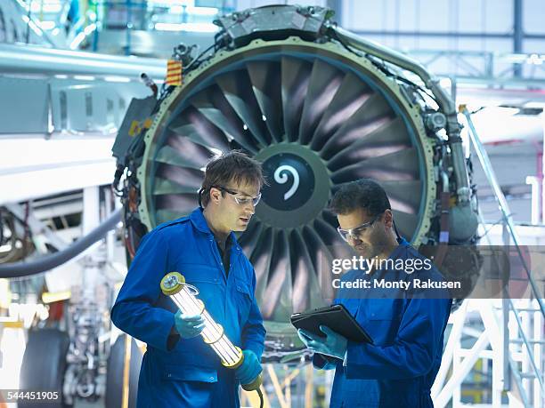 aircraft engineers discussing maintenance details on digital tablet in front of jet engine in aircraft maintenance factory - digital techniques ストックフォトと画像