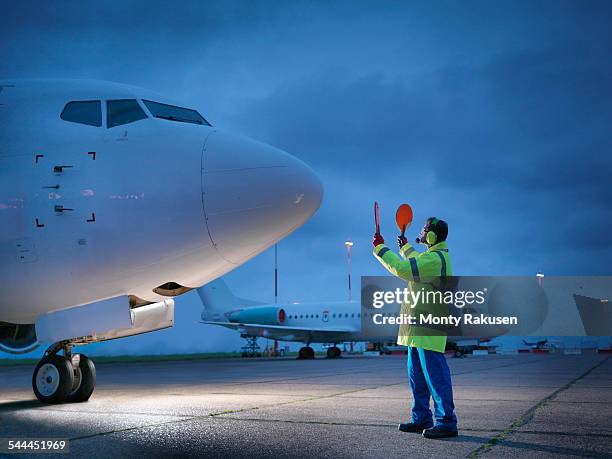 airport worker guiding aircraft on runway at night - runway night stock pictures, royalty-free photos & images