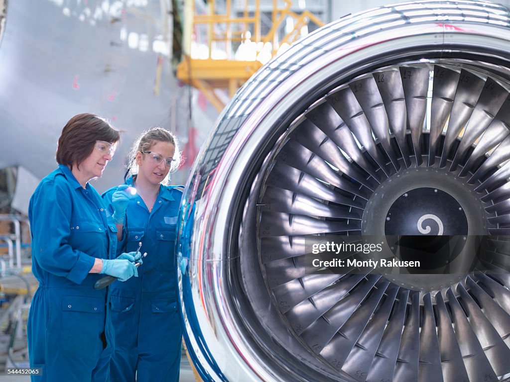 Female engineers working on engine in aircraft maintenance factory