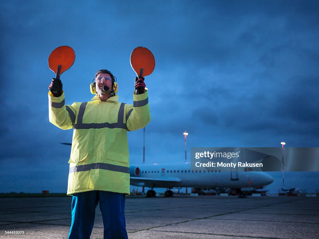 Airport worker guiding aircraft on runway at night