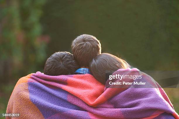 siblings wrapped in blanket in garden - family no faces stockfoto's en -beelden