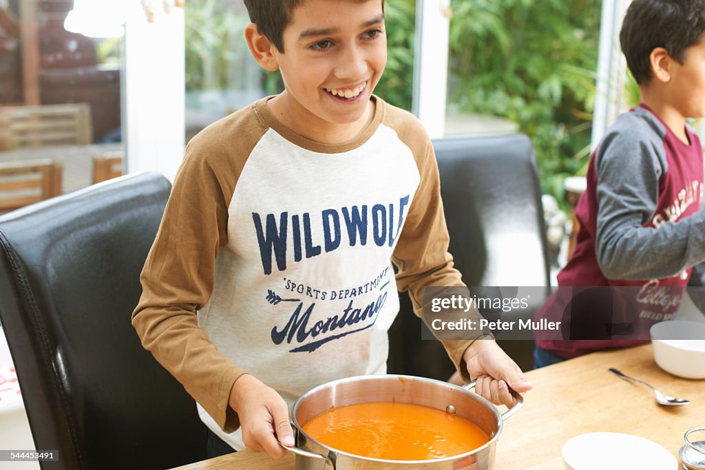 Boys at kitchen table holding pan of tomato soup