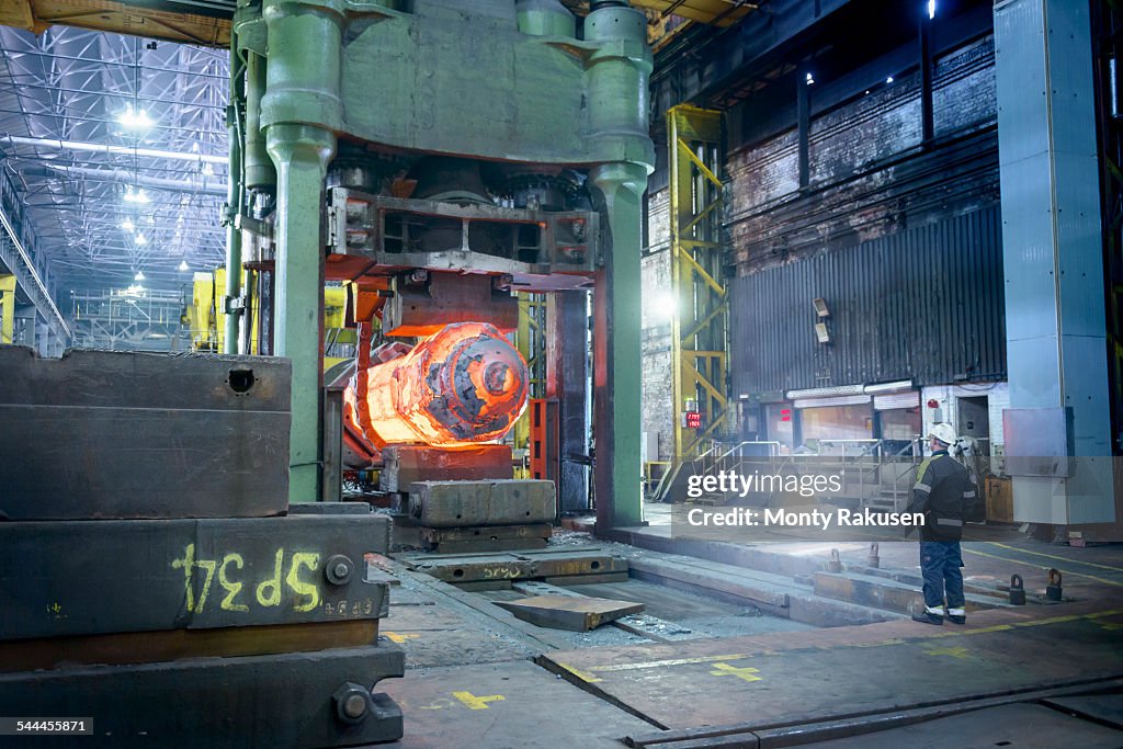 Steelworker inspects hot steel in forging press in steelworks