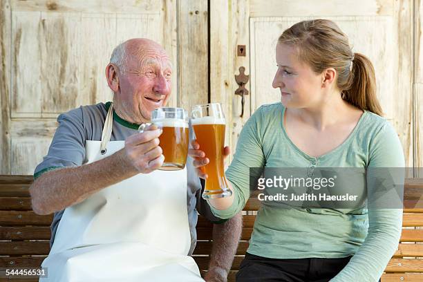 senior man and young woman toasting with beer - bavaria beer stock pictures, royalty-free photos & images