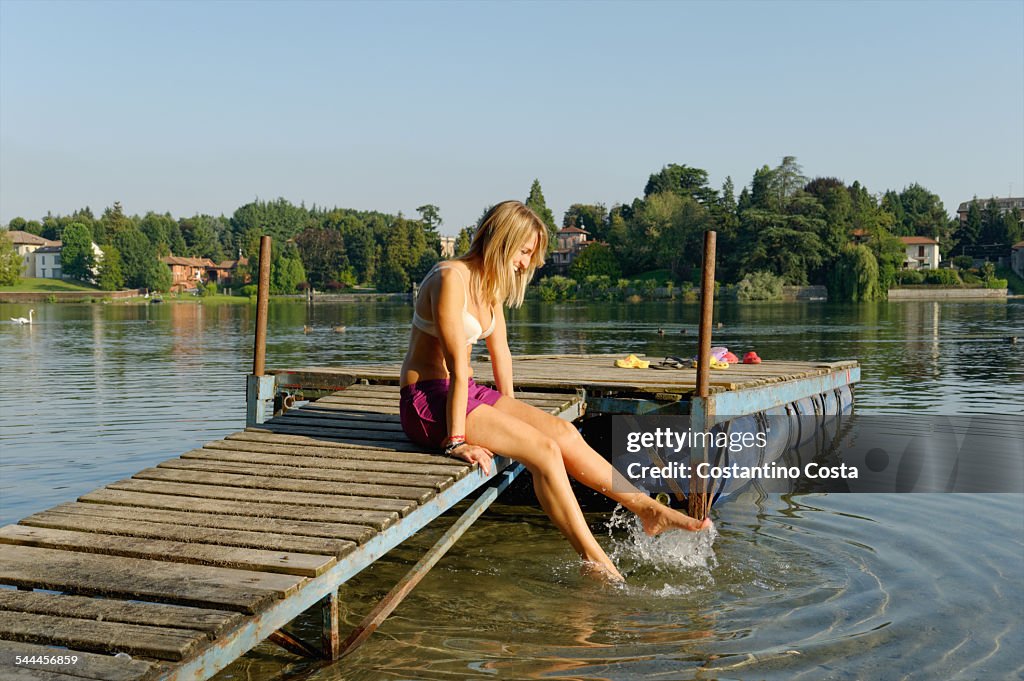 Partially dressed mid adult woman, sitting on jetty, dipping feet in water