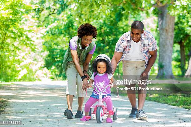 幸せな母と父と娘を教える幼児で三輪車 - 三輪車 ストックフォトと画像