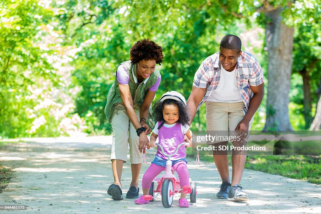 Feliz Mãe e pai ensinando sua filha bebê para passeio triciclo