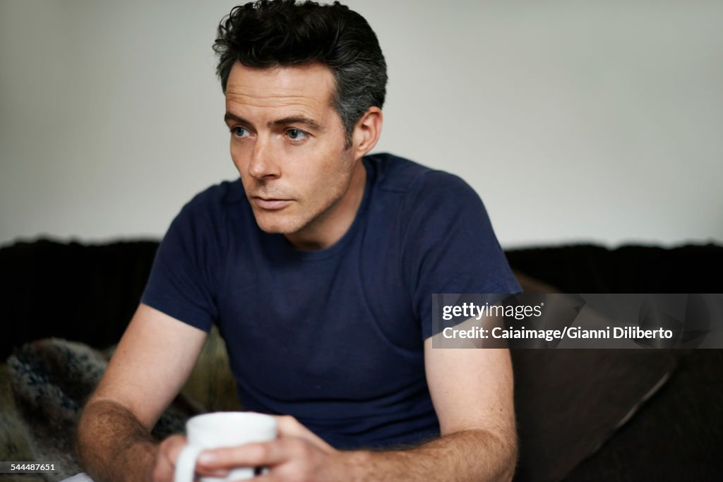 Man sitting on sofa holding mug looking sad