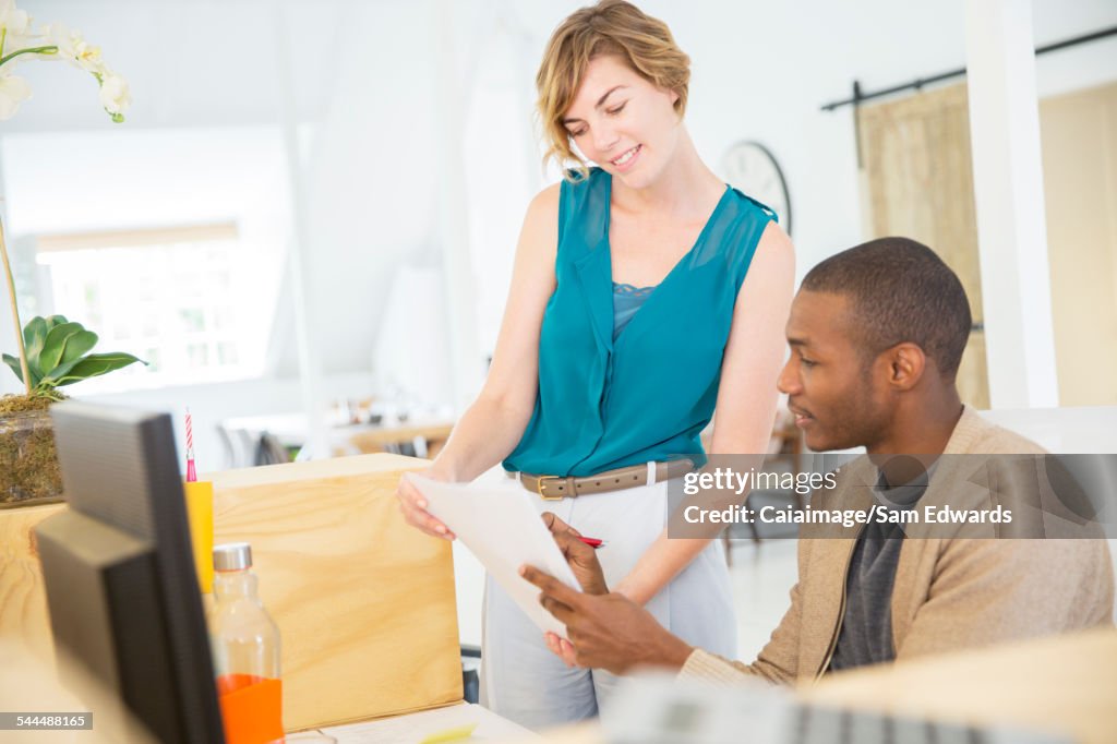 Woman and man looking at documents, talking and smiling in office