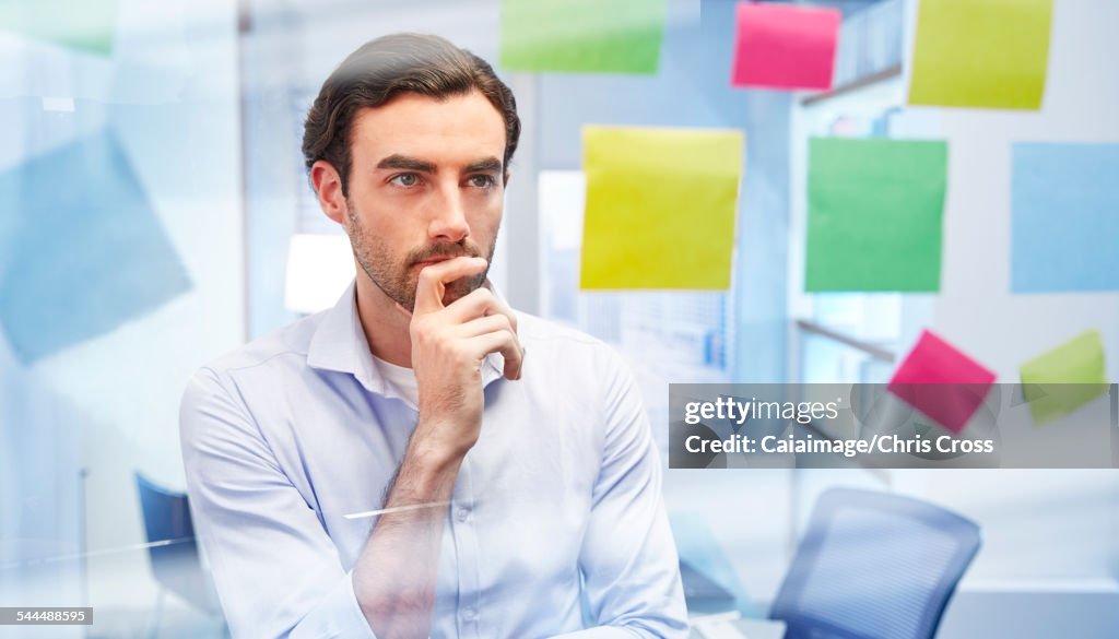 Office worker behind glass with colorful sticky notes thinking
