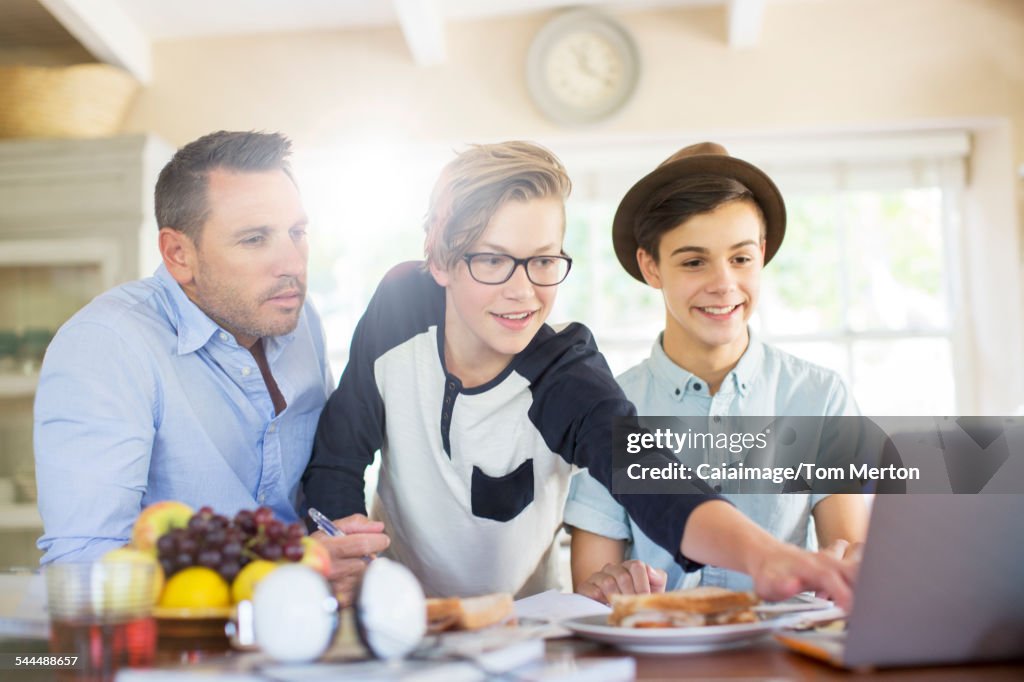 Teenage boys with father using laptop in dining room