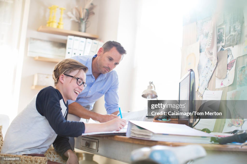 Father helping teenage son doing his homework in room