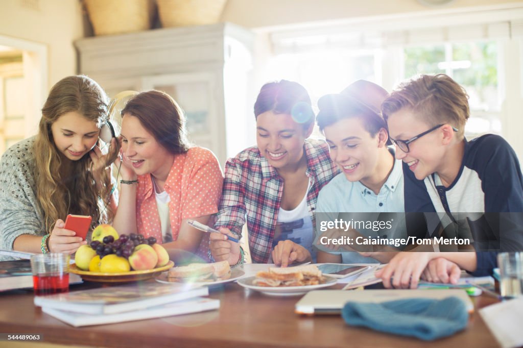 Group of teenagers using electronic devices at table in dining room