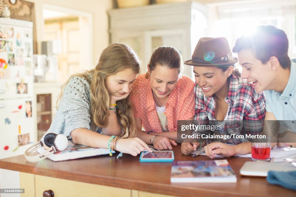 Grupo de adolescentes usando juntos la tableta digital en la mesa de la cocina