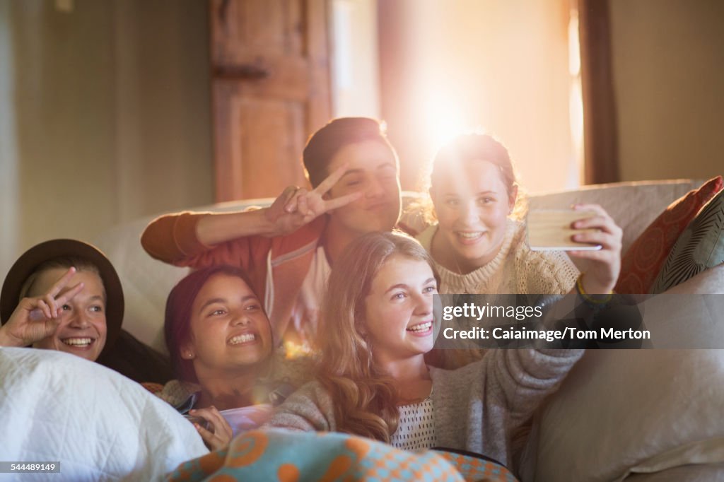 Group of smiling teenagers taking selfie on sofa in living room
