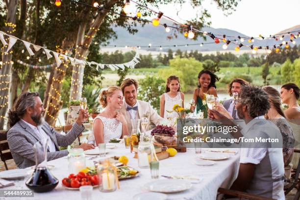 Jeune couple et leurs invités assis à table pendant la réception de mariage dans le jardin