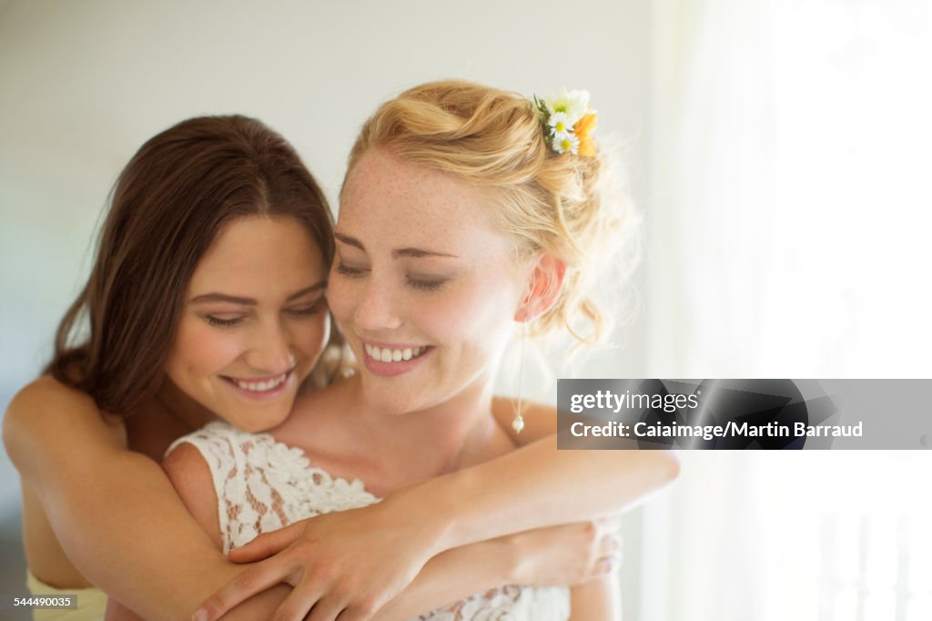 Bridesmaid embracing bride in bedroom