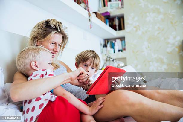 mother with her sons watching tablet in bed - boy in pajamas and mom on tablet stock-fotos und bilder