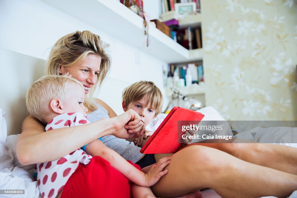 Mother with her sons watching tablet in bed