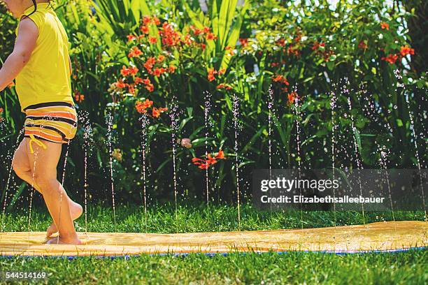 young girl (2-3) running through water - backyard water slide stock pictures, royalty-free photos & images