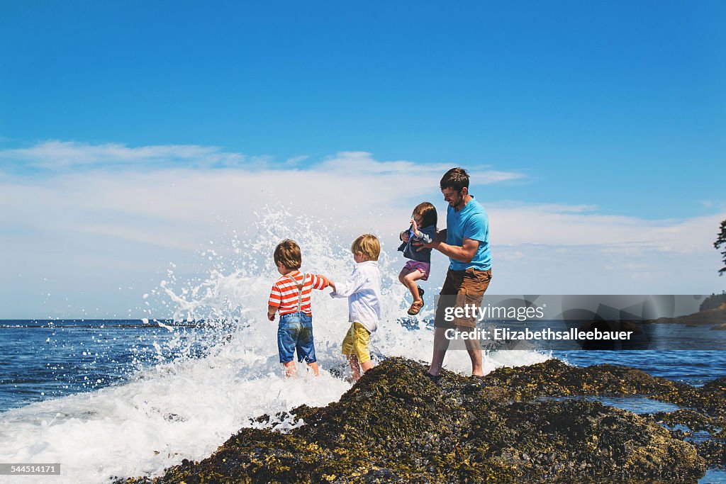 Father and three children (2-3, 4-5) playing in waves